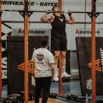 Athletes performing pull-ups in a CrossFit competition, judged by officials, showcasing strength and endurance.